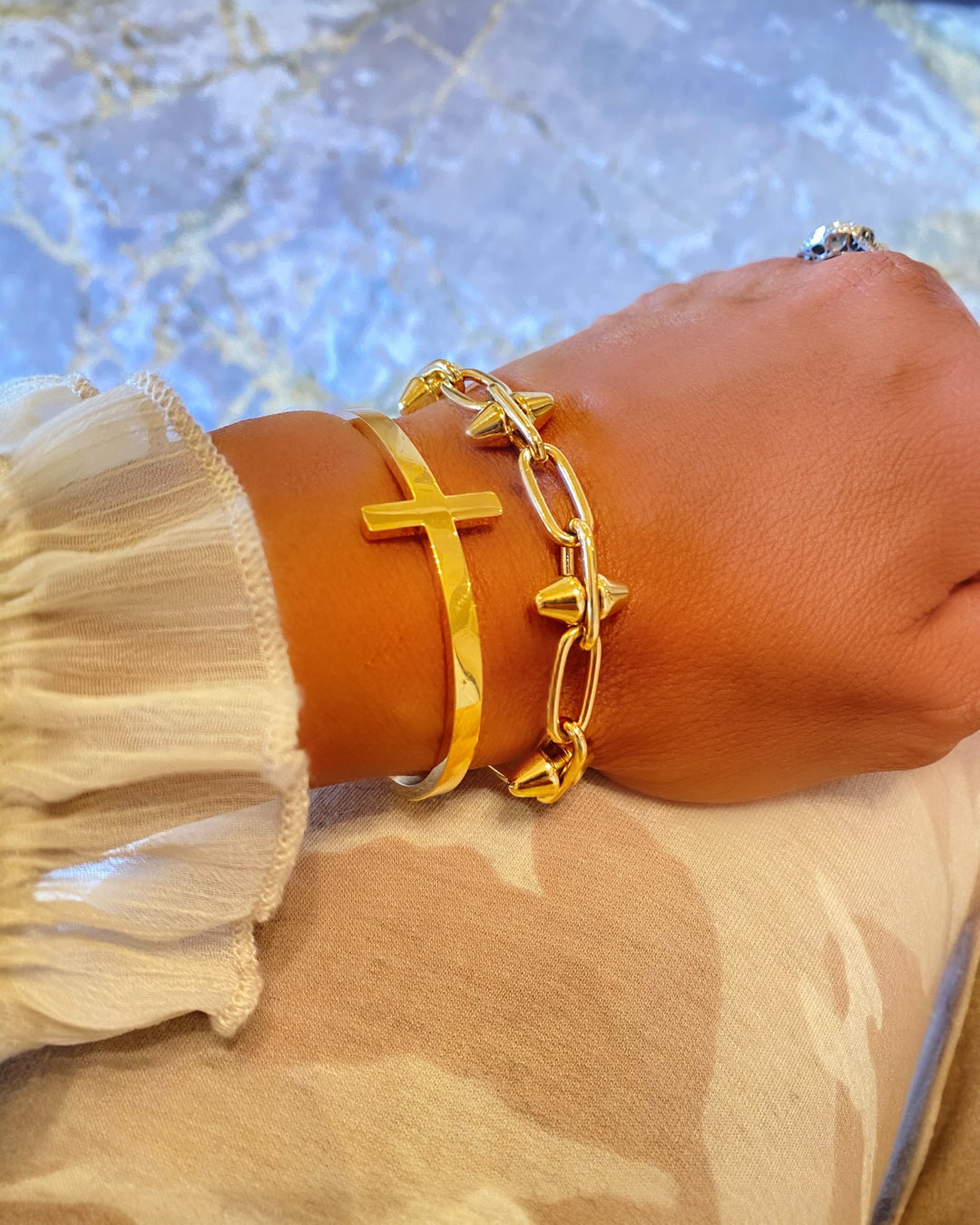 Gold bracelet with a cross design on a wrist against a textured background