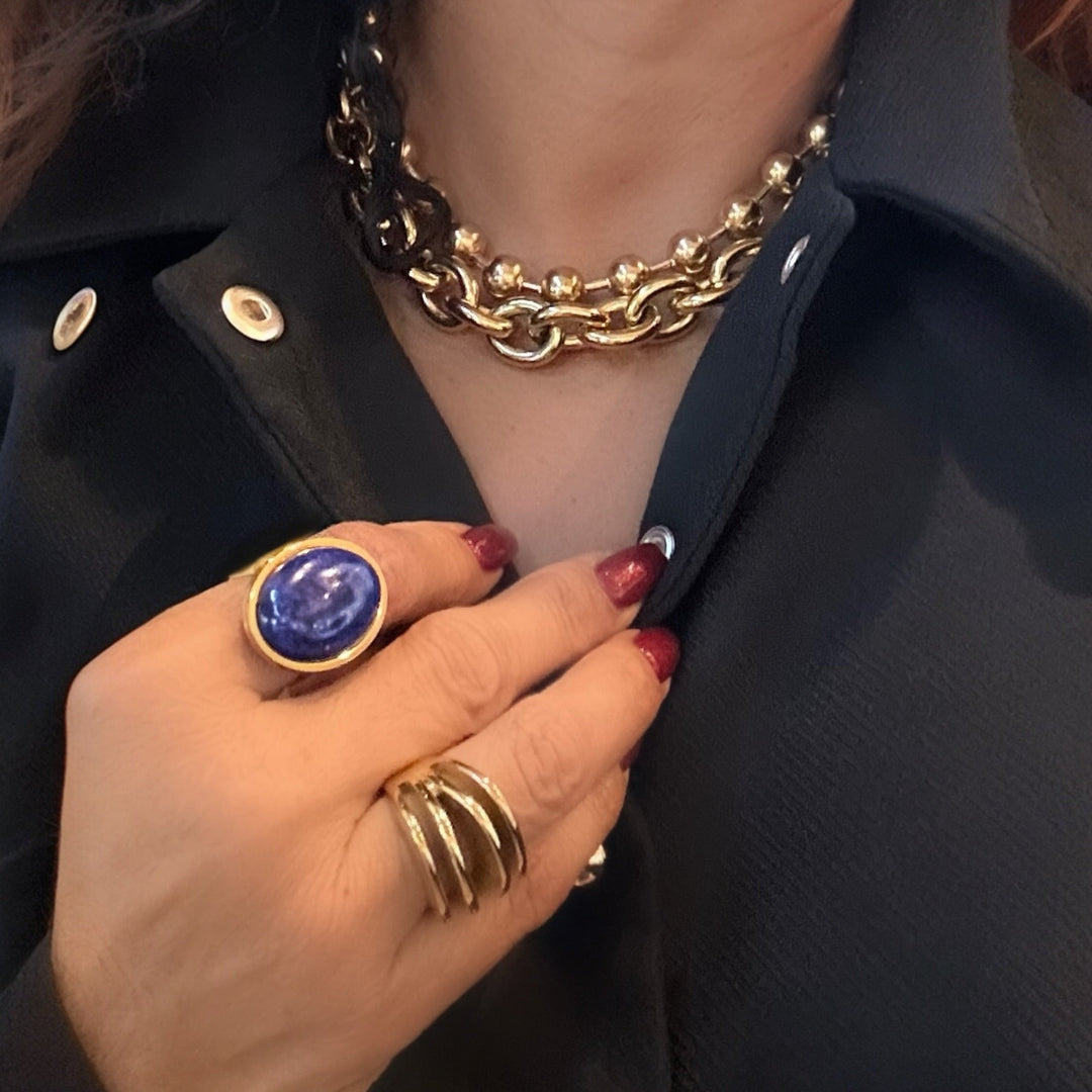 Hand wearing a gold ring with a blue stone on a dark background