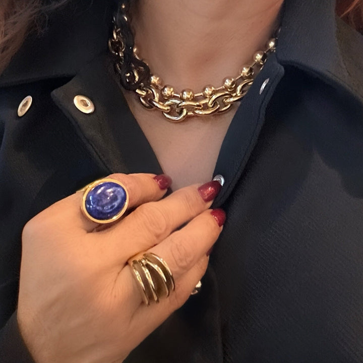 Hand wearing a gold ring with a blue stone on a dark background