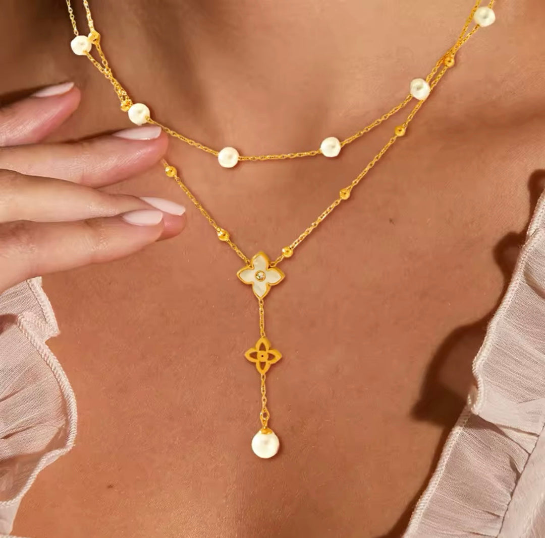 Gold necklace with floral and round pendants on a person wearing a sheer top.