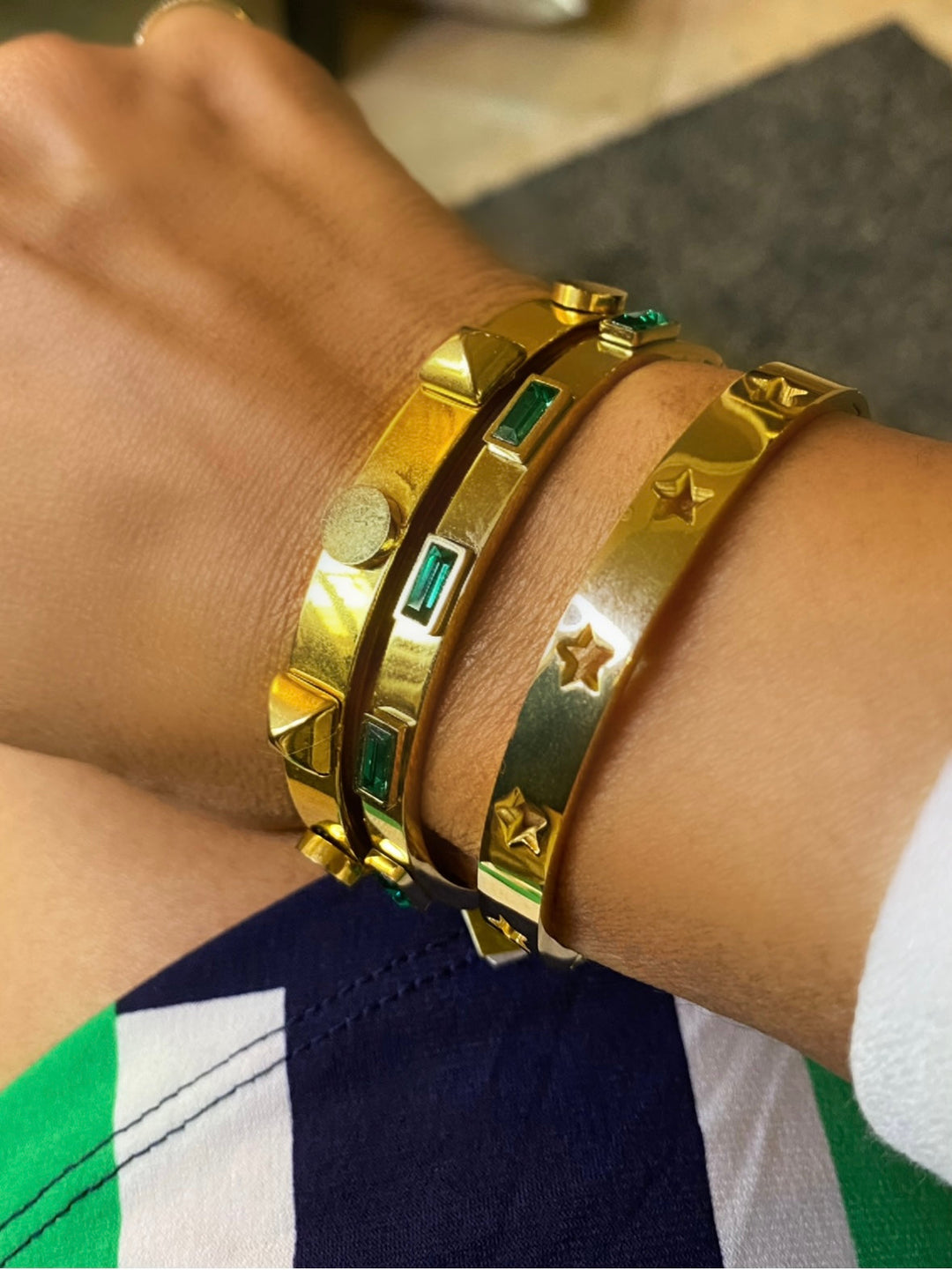 Gold bracelets with star and green gemstone designs on a wrist.