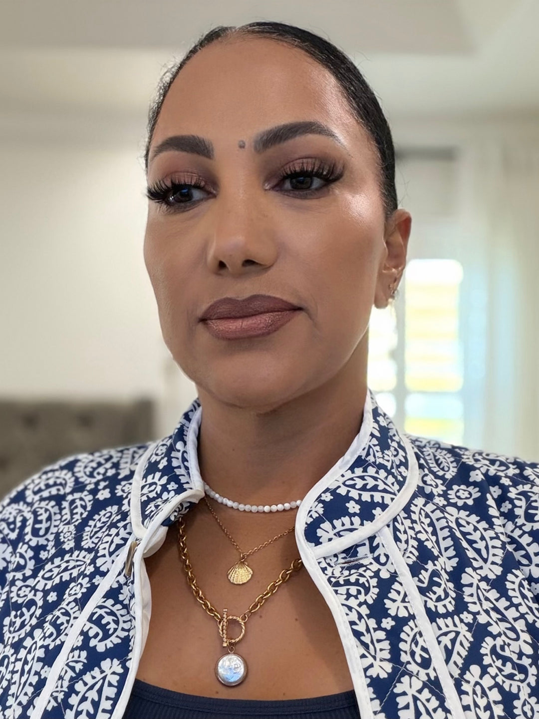 Woman wearing a blue and white patterned jacket with layered pearl necklaces indoors.