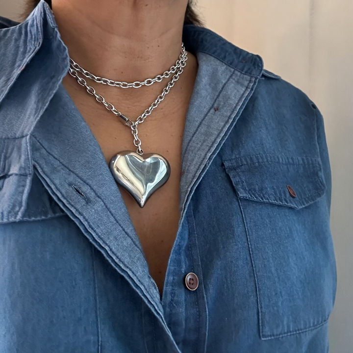 Person wearing a blue denim shirt with a silver heart-shaped pendant necklace.