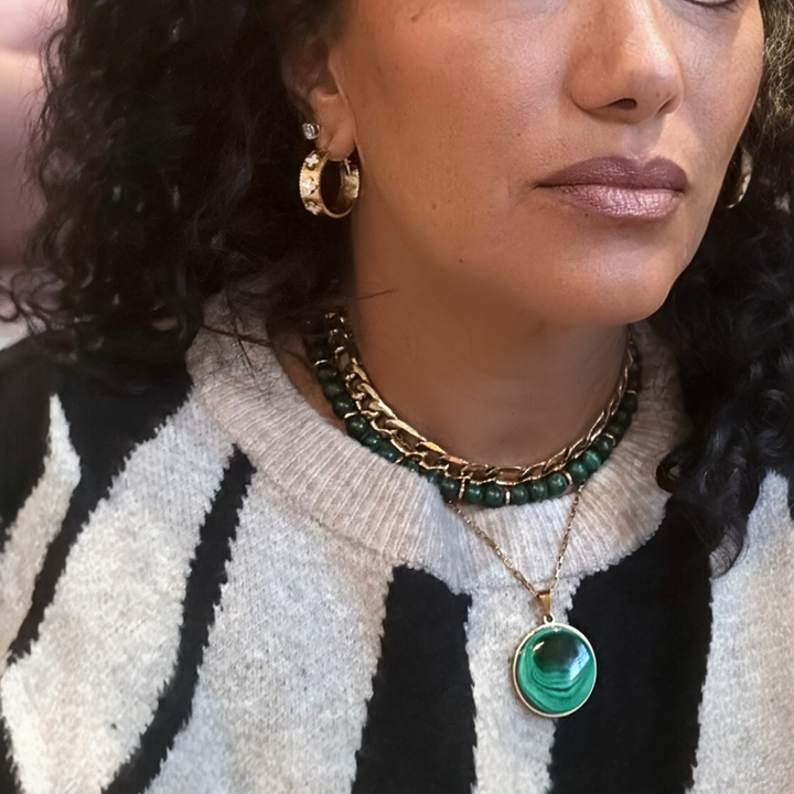 Close-up of a person wearing gold earrings and a necklace with a green pendant.