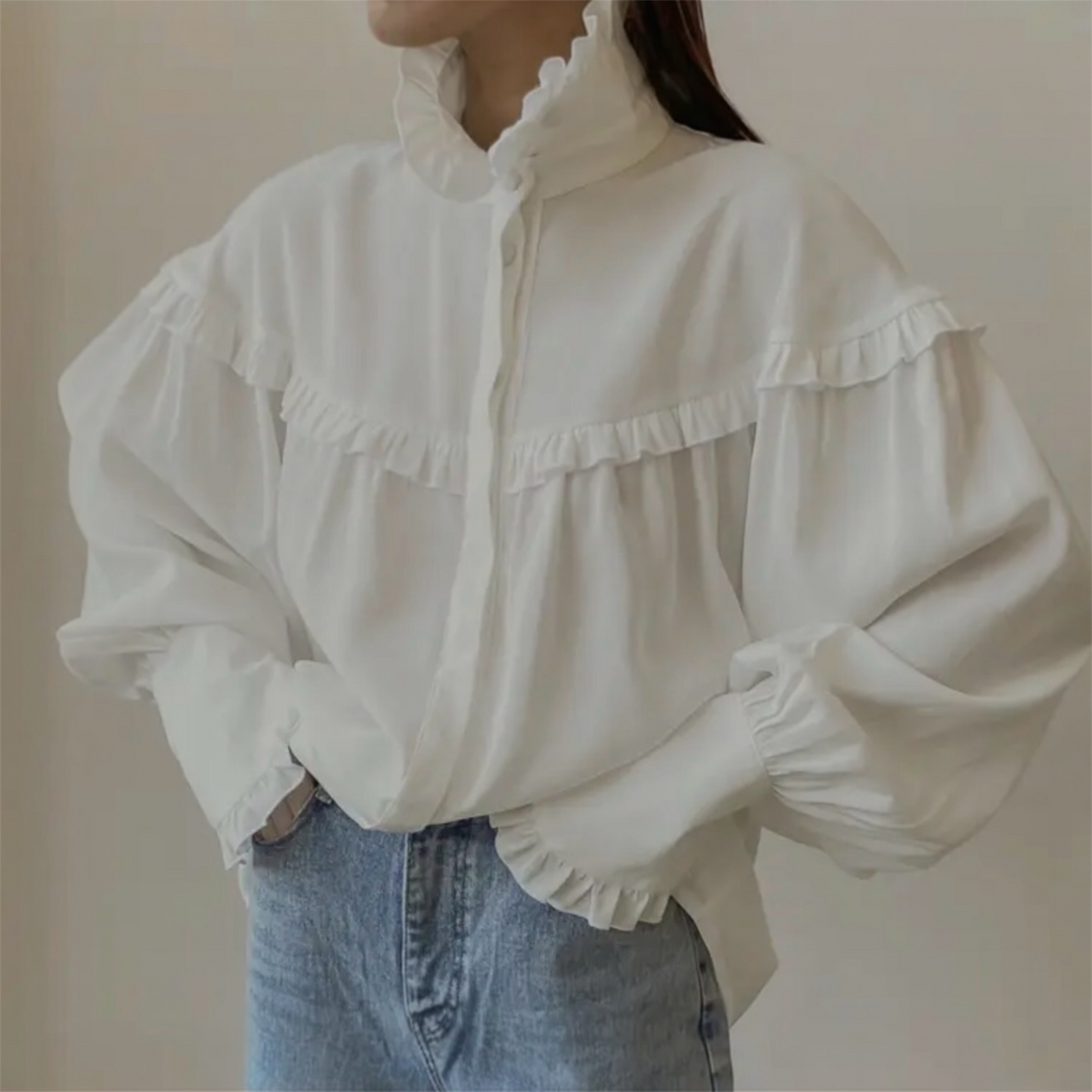 White blouse with ruffled details worn by a person against a plain background