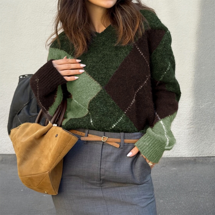 Person wearing a green and brown argyle sweater holding a brown bag against a neutral background