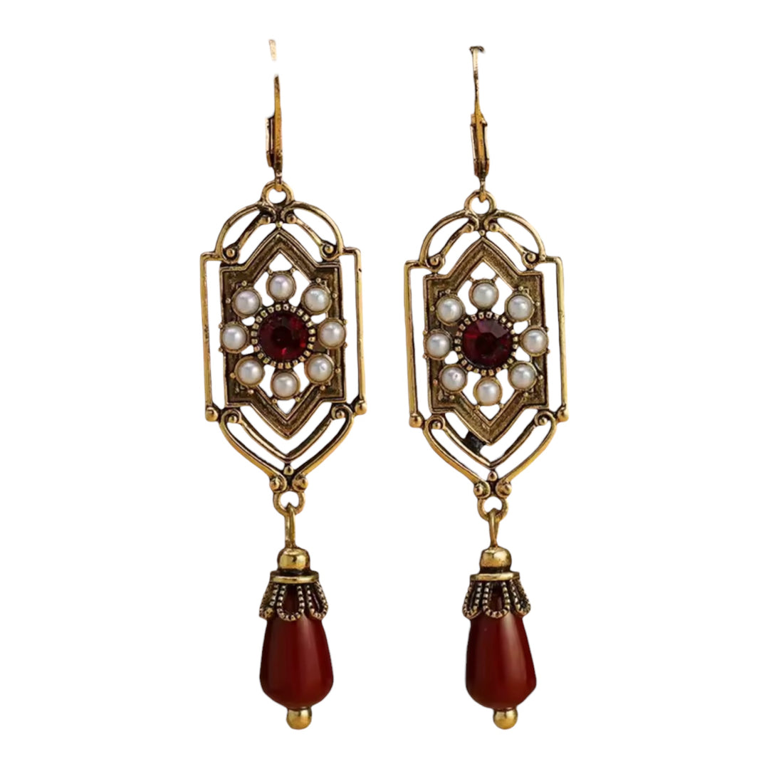 Pair of ornate earrings with gold frames, red beads, and pearl-like stones on a white background.