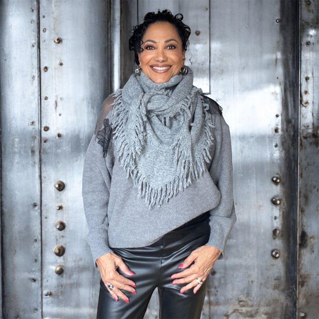 Woman wearing a gray sweater and scarf standing against a metallic background