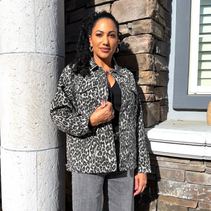 Woman wearing a leopard print jacket standing against a stone wall.