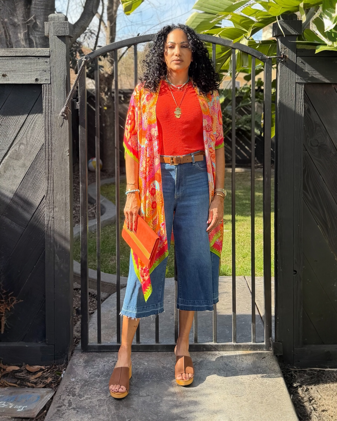 Colorful bohemian cotton kimono cardigan with vibrant coral, pink, orange, and lime floral print, open front design, and flowy silhouette styled over denim and a red top.