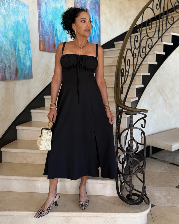 Woman in a black dress standing on a staircase with decorative railings and artwork in the background.