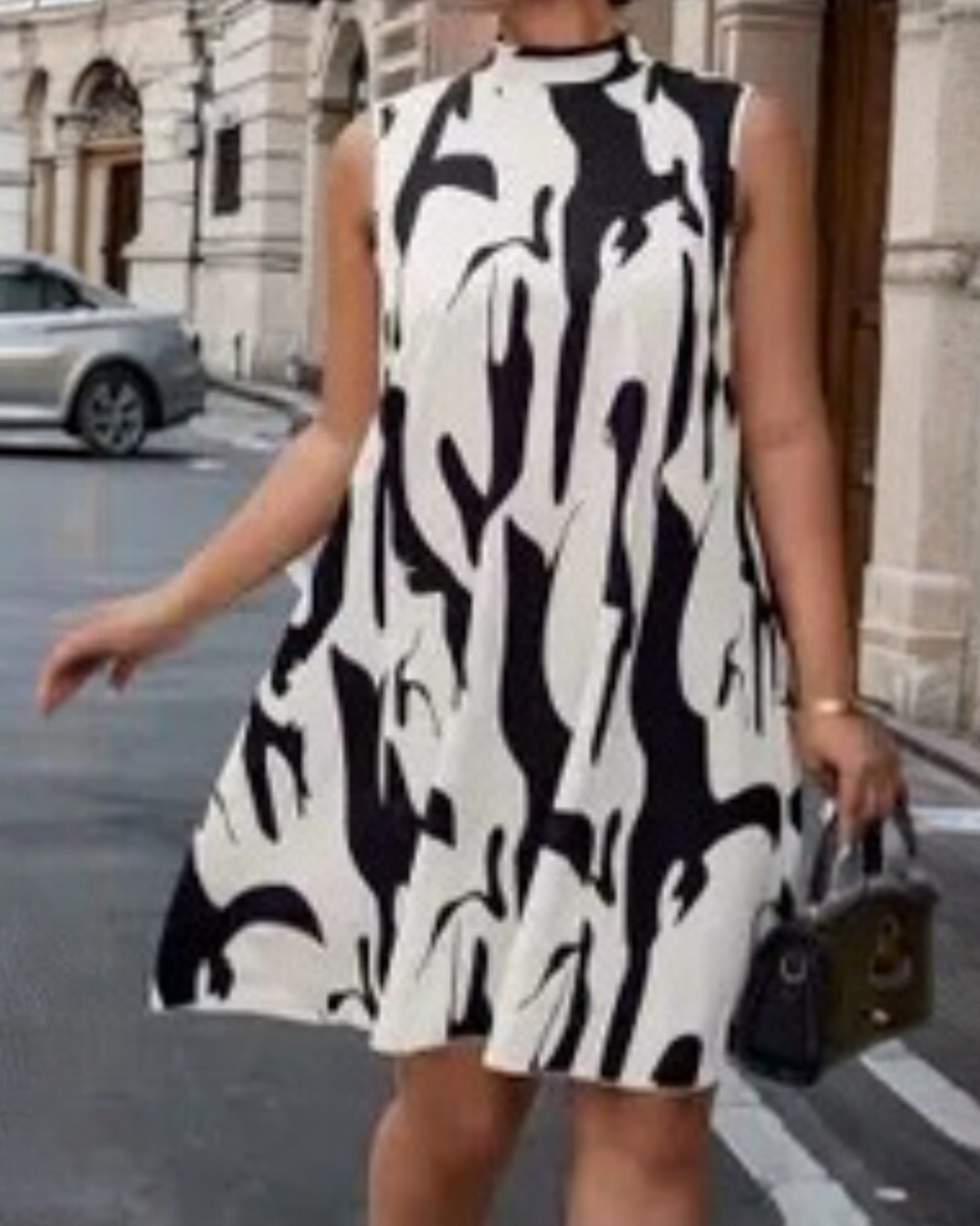 Black and white abstract print sleeveless swing dress styled with a small black handbag.