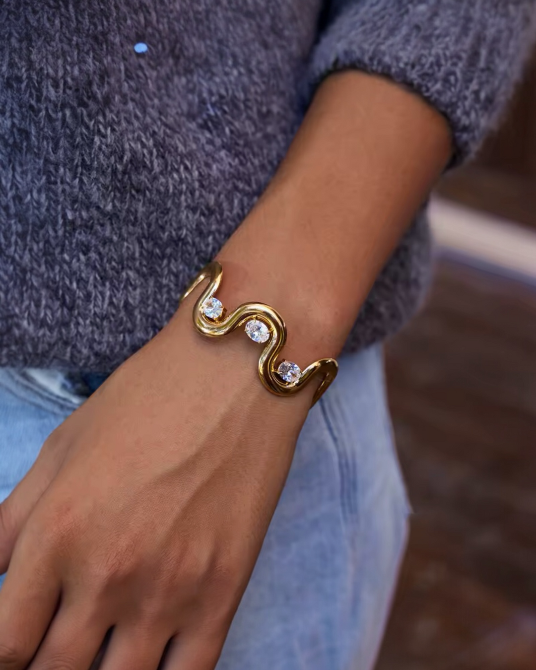 Gold wave cuff bracelet with three crystal stones worn on wrist.