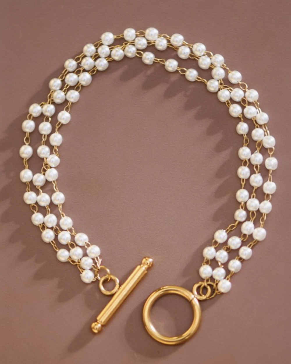 Layered pearl toggle bracelet with multi-strand pearls and gold chain links featuring a large gold toggle clasp.