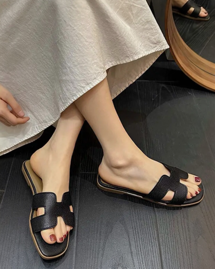 Black textured slide sandals with cutout strap design styled with a neutral dress.