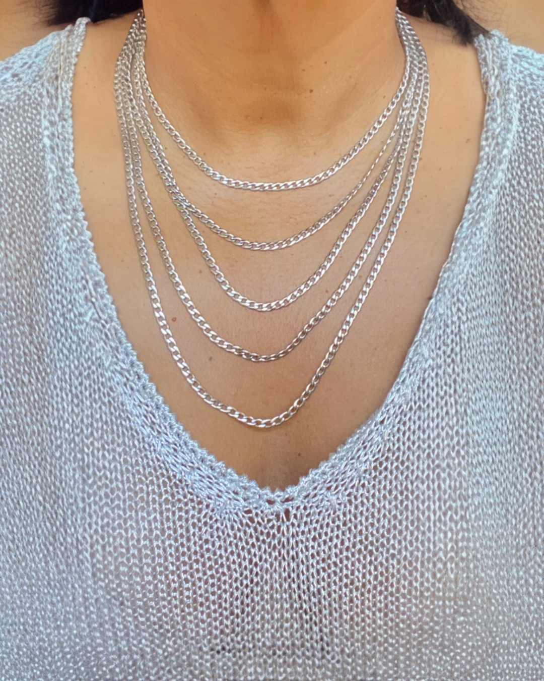 Silver chain necklaces on a person wearing a light blue top.