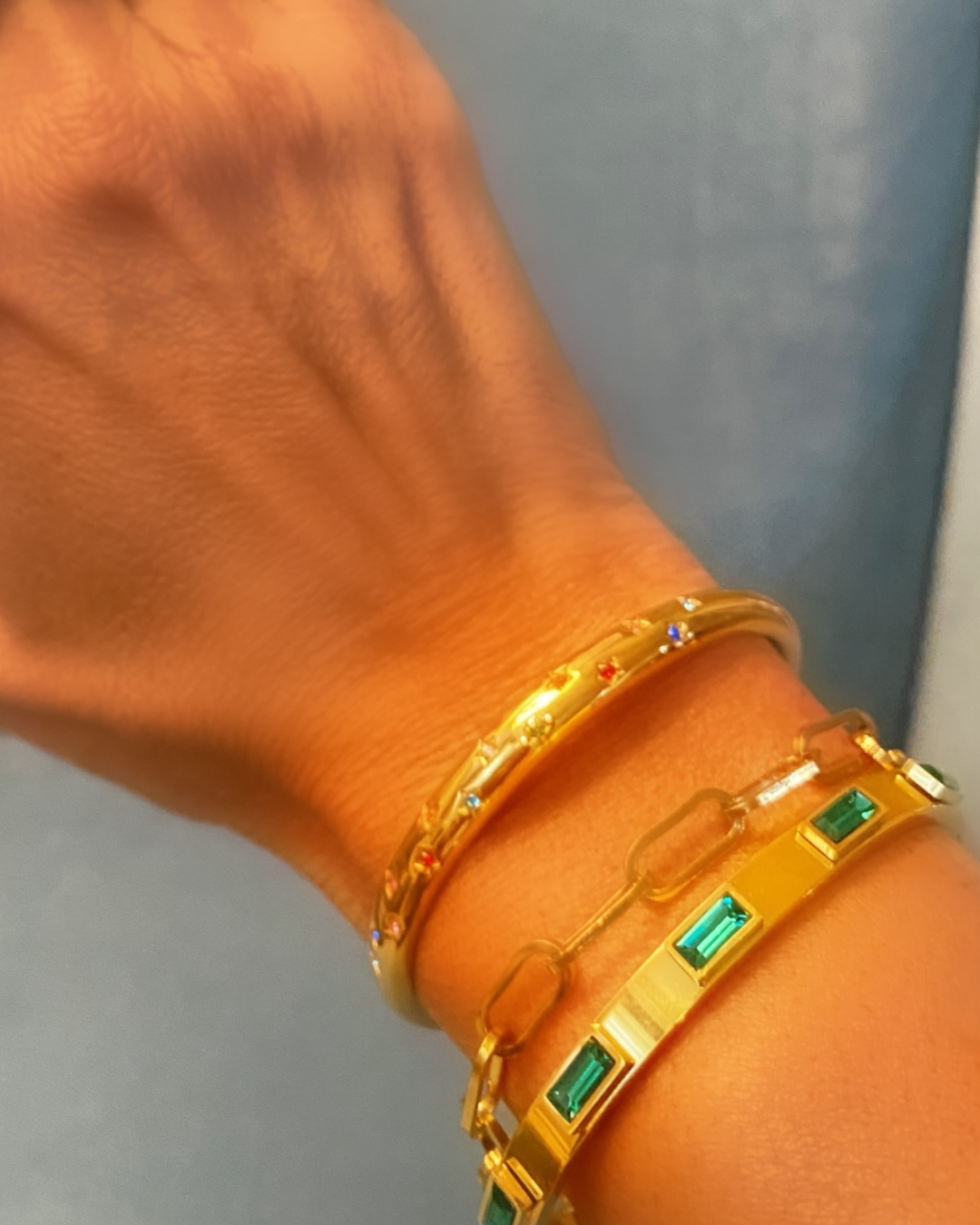 Gold bracelets with rainbow stones on a wrist against a neutral background