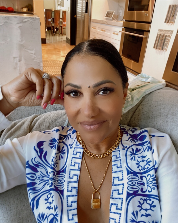 Woman wearing a blue and white patterned top with gold padlock necklace jewelry in a kitchen setting