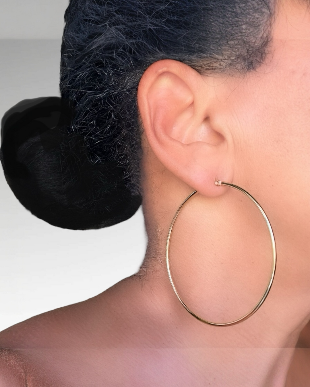 Close-up of a person wearing a gold hoop earring with a neutral background
