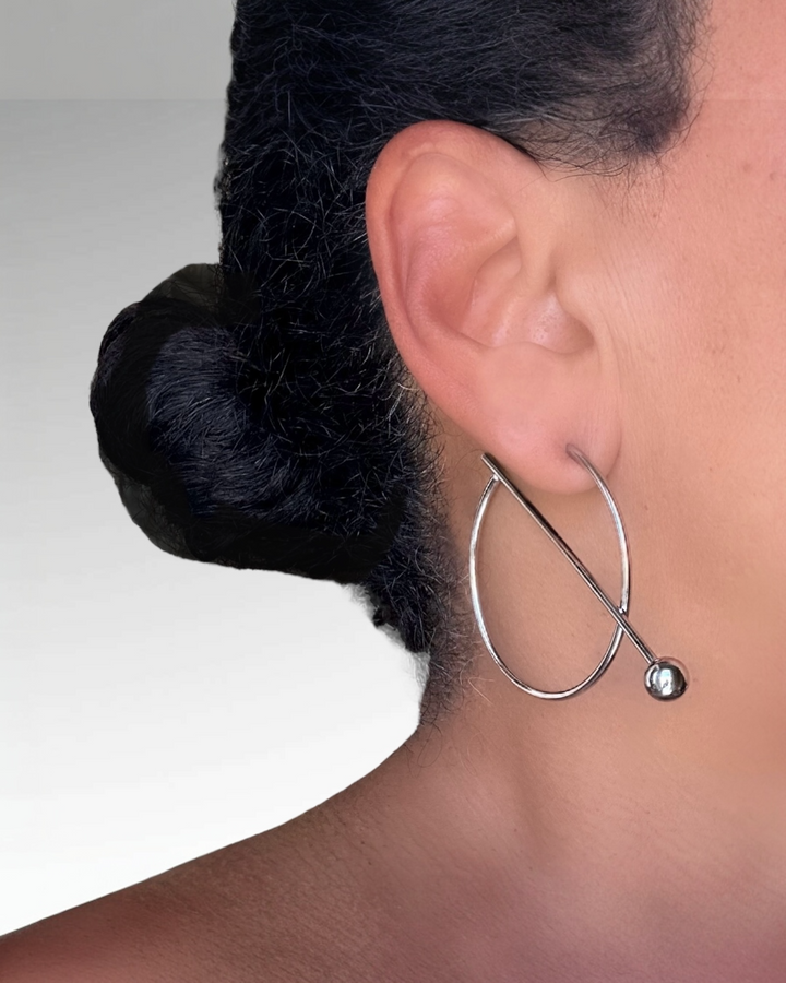 Silver hoop earring with a small round pendant worn by a person with dark hair.