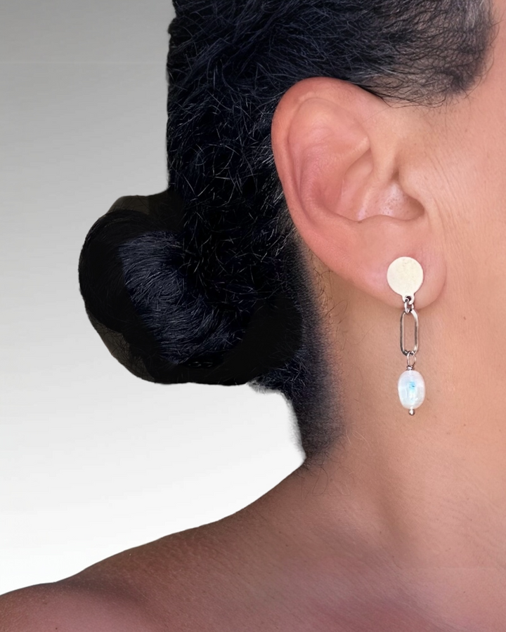 Close-up of an ear wearing a silver earring with a central pearl, against a neutral background.