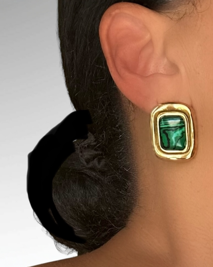 Gold earring with green gemstone worn by a person with dark hair.