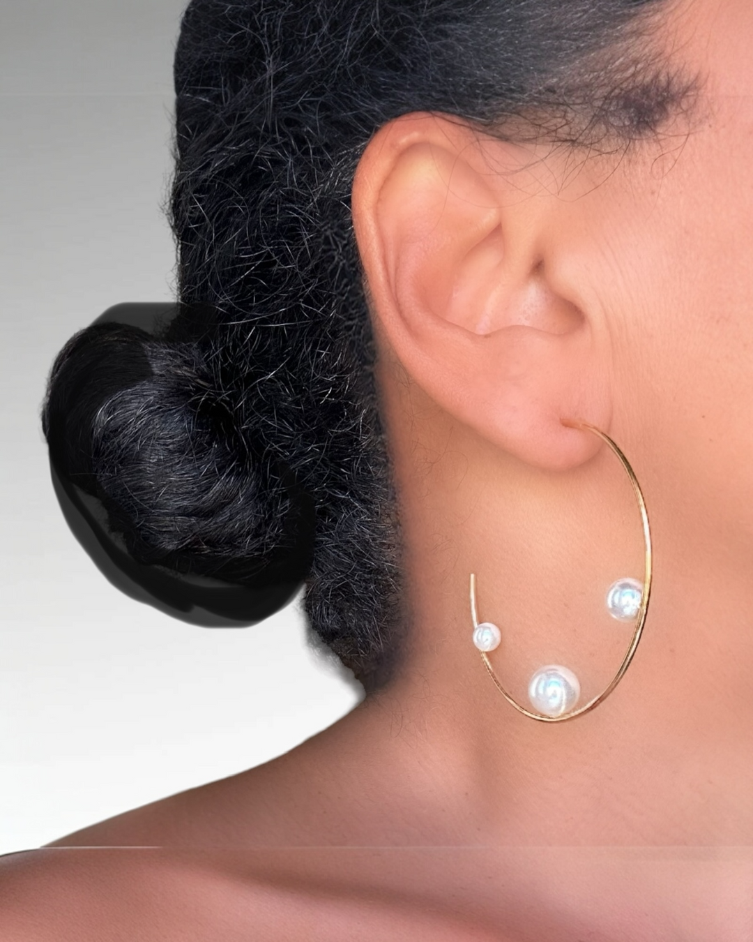 Close-up of a person wearing a gold hoop earring with pearls on a plain background