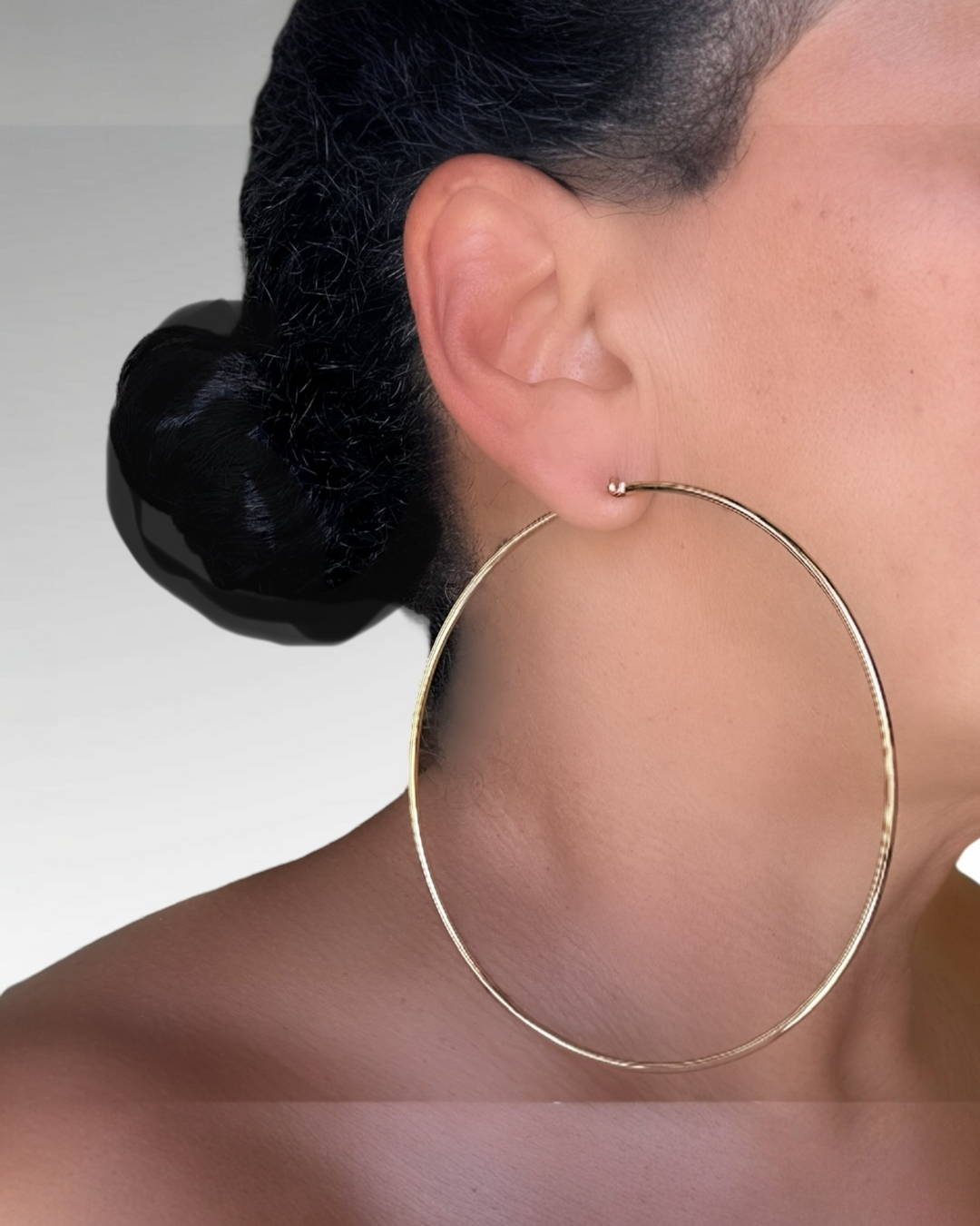 Close-up of a person wearing a gold hoop earring with a neutral background