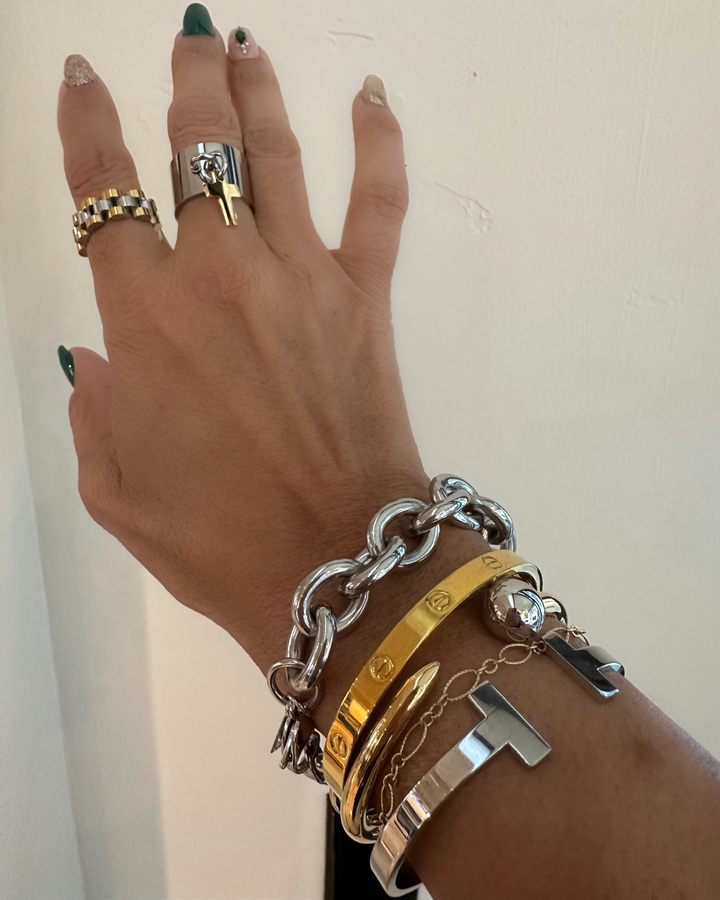 Hand wearing multiple bracelets and rings on a plain background