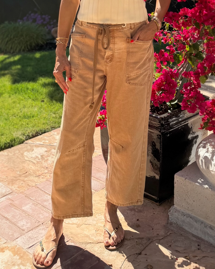 Person wearing tan barrel jeans standing on a stone path with flowers in the background
