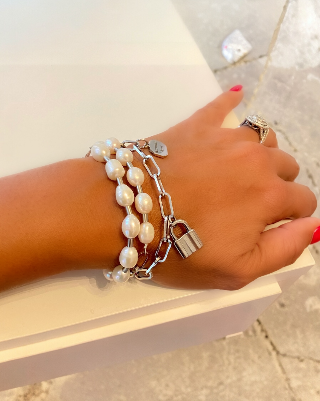 Hand wearing bracelet with pearls and a lock charm on a light background