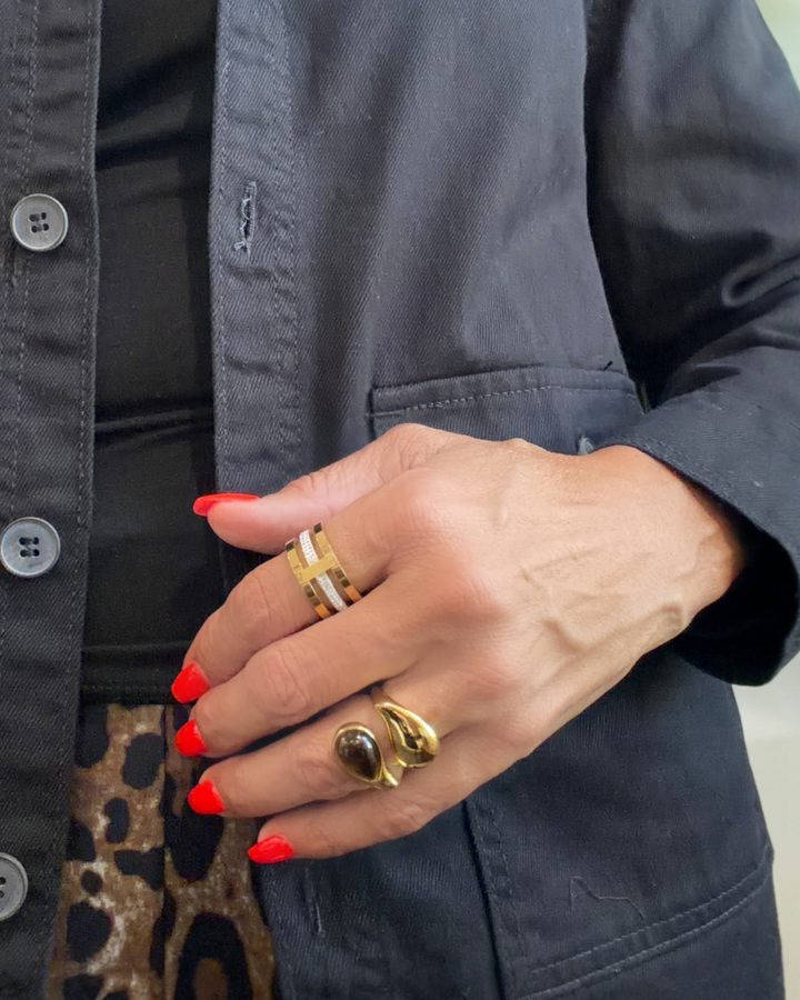 Hand with red nail polish wearing gold tigers eye rings on a dark jacket background
