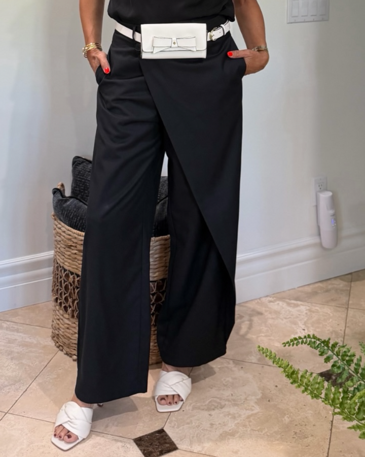 Person wearing black wide-leg pants with a white belt and white sandals in a room.