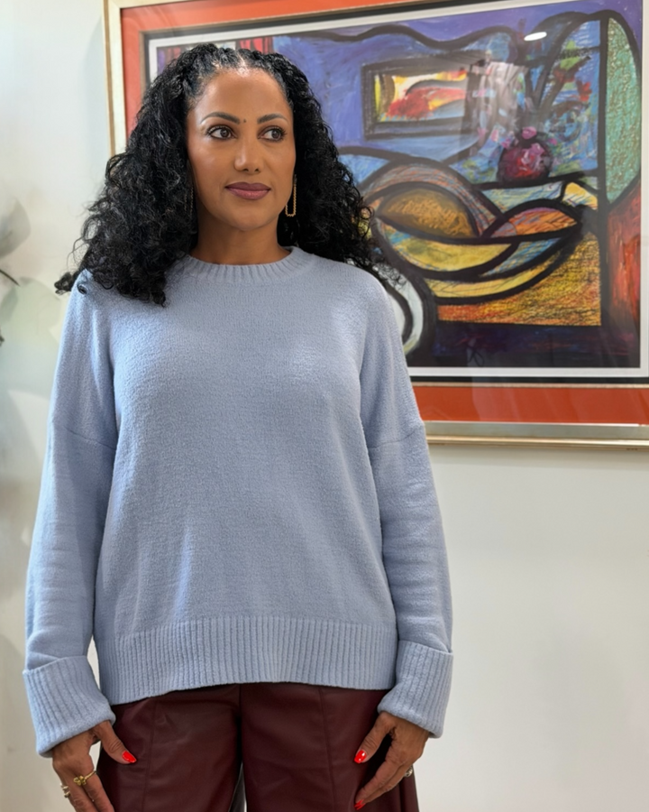 Woman wearing a light blue sweater standing in front of a colorful abstract painting.