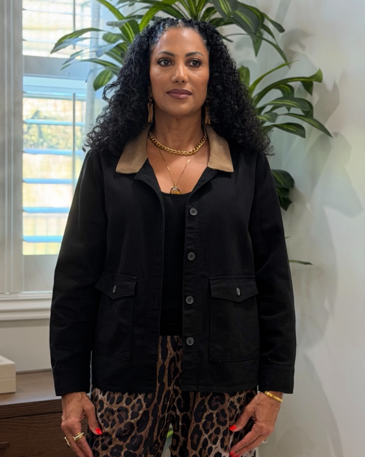 Woman wearing a black barn jacket and leopard print pants indoors with plants in the background
