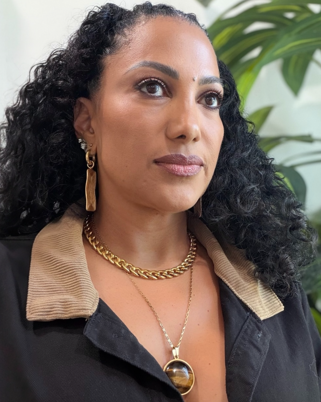 Woman wearing gold necklace jewelry with a blurred green plant background