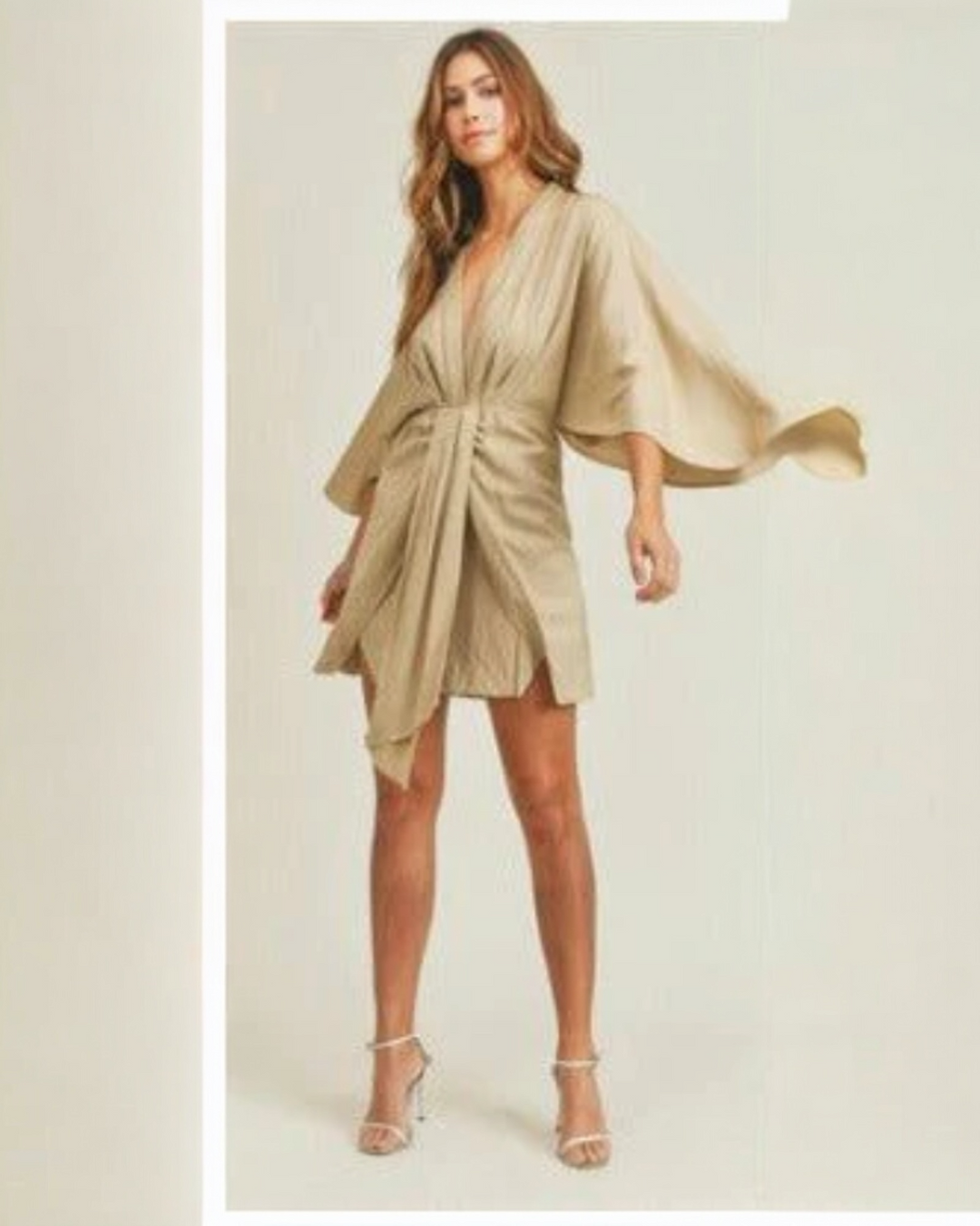 Woman wearing a beige dress with flowing sleeves on a plain background