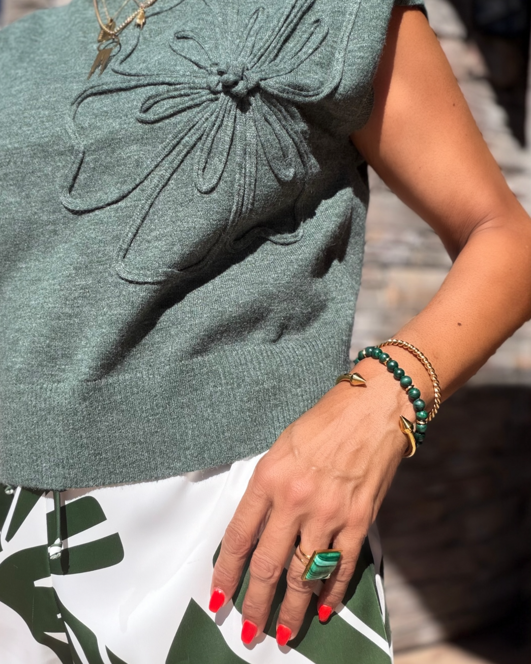 Green sleeveless top with floral details worn by a person, wearing a gold twisted bracelet