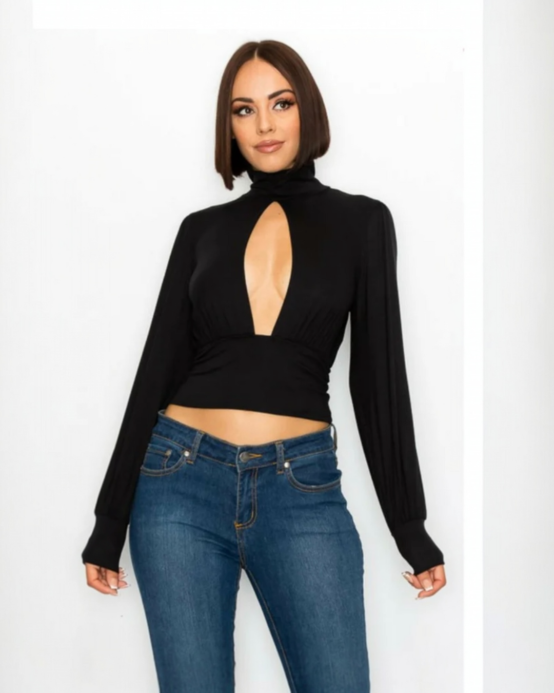 Woman wearing a black long-sleeve top with a cutout design and blue jeans on a white background
