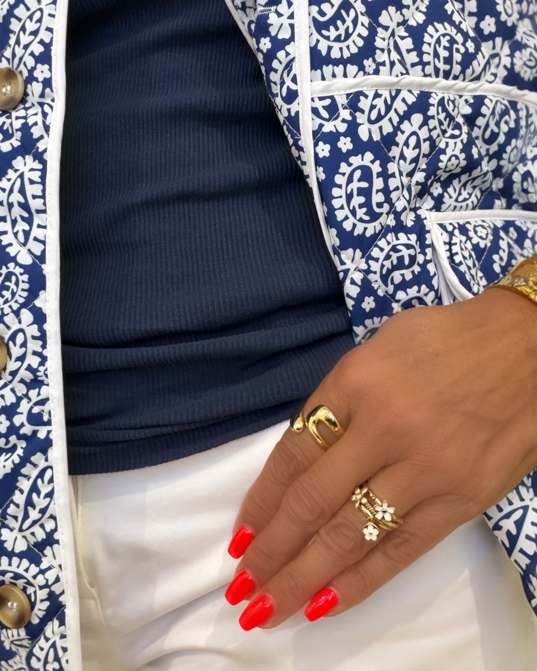 Close-up of a hand wearing gold rings with red nail polish, against a blue and white patterned background