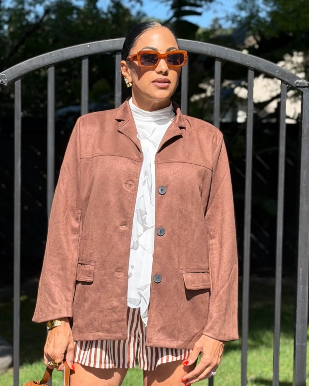 Woman wearing a brown blazer, white shirt, and striped shorts outdoors.