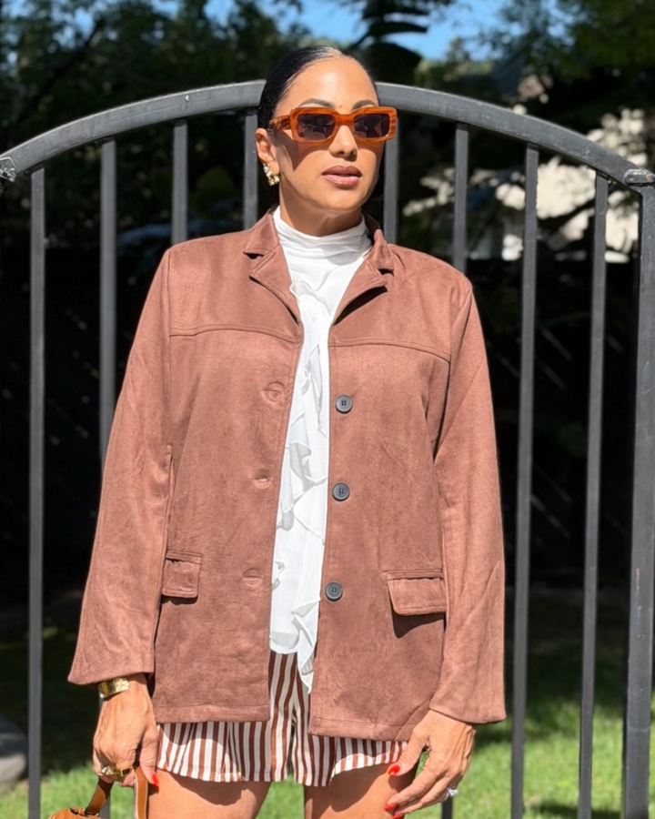 Woman wearing a brown blazer, white shirt, and striped shorts outdoors.