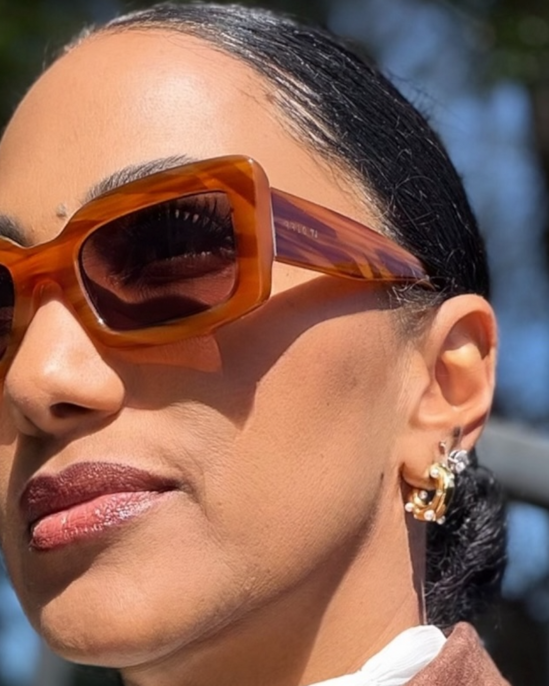 Close-up of a person wearing pearl huggie earrings with a blurred background