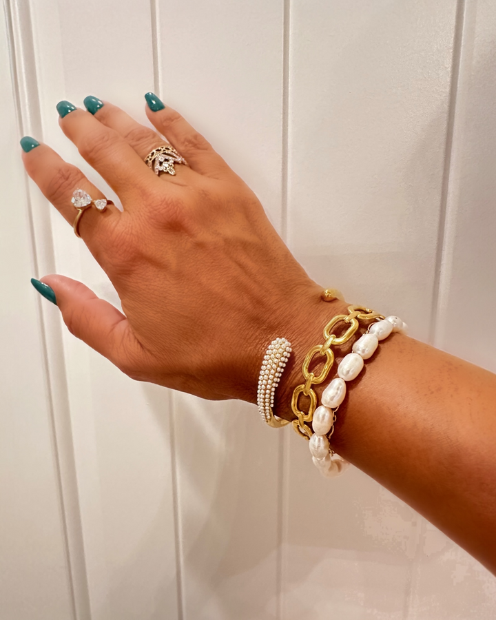 Hand wearing multiple pearl bracelets with a white background