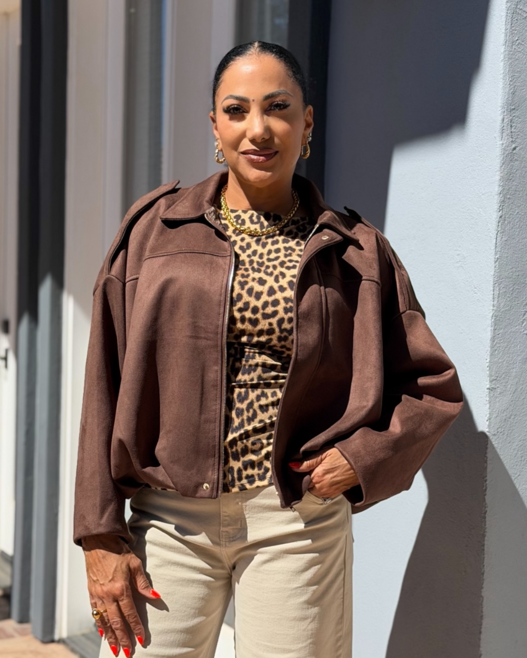 Woman wearing a brown jacket and leopard print top standing outdoors.