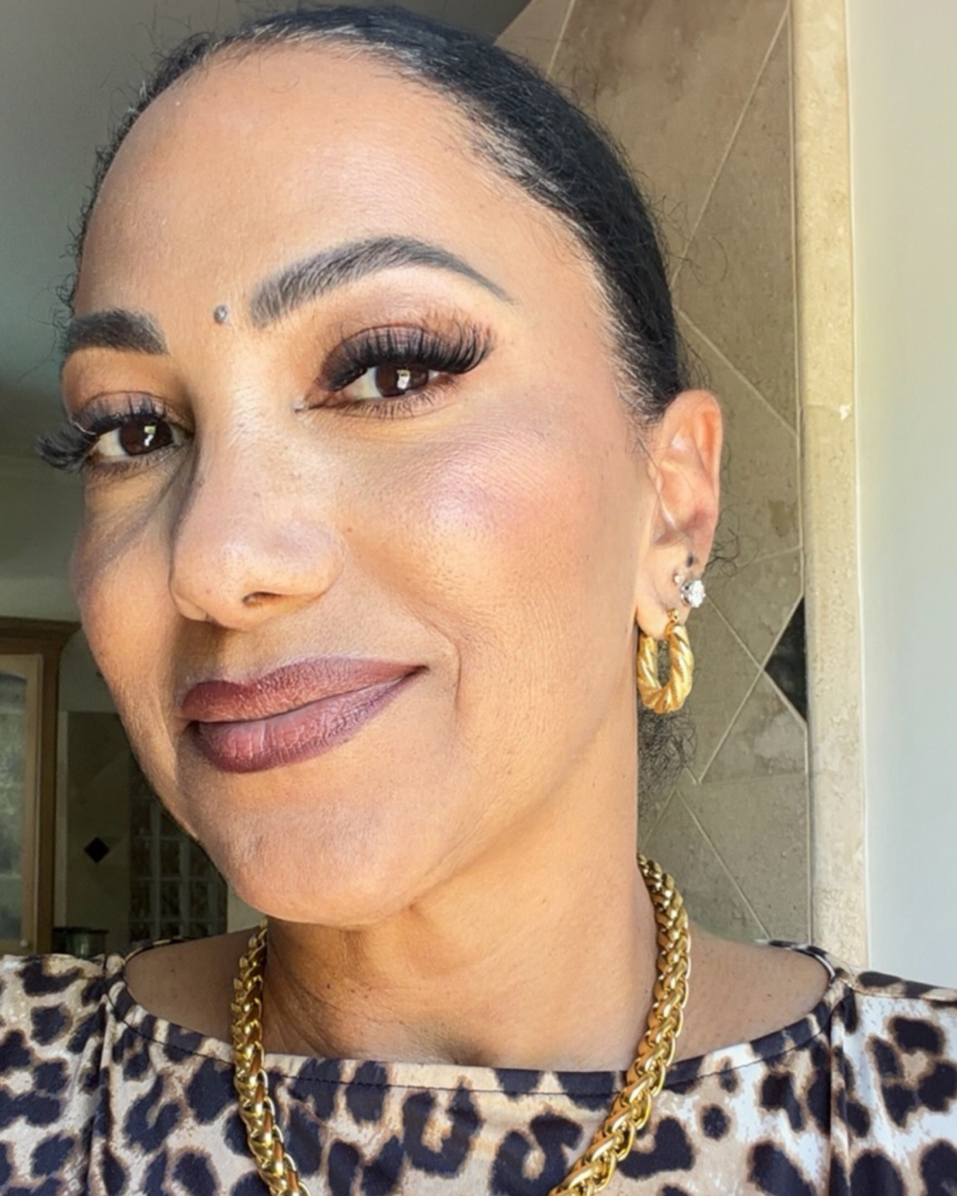 Woman wearing gold hoop earrings and a leopard print top indoors.