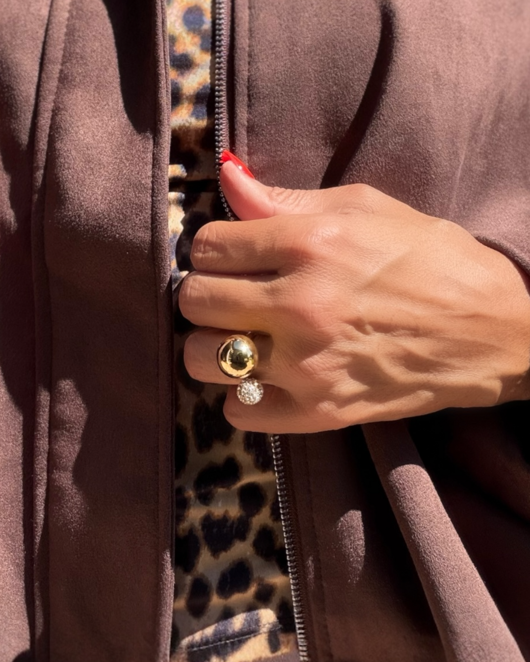 Close-up of a hand with a gold ring on a brown garment with a leopard print zipper.