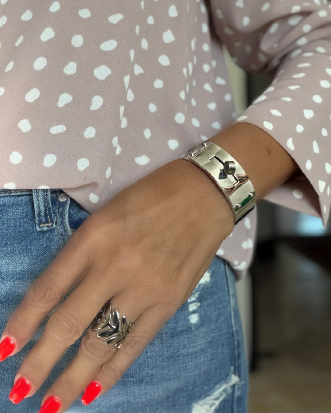 Close-up of a hand wearing a silver bracelet and ring, with polka dot shirt and jeans.