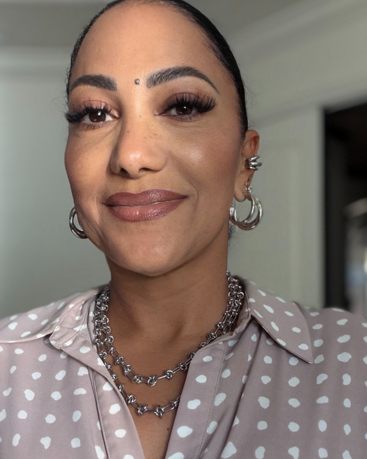 Woman wearing a polka dot blouse with layered necklaces and hoop earrings.