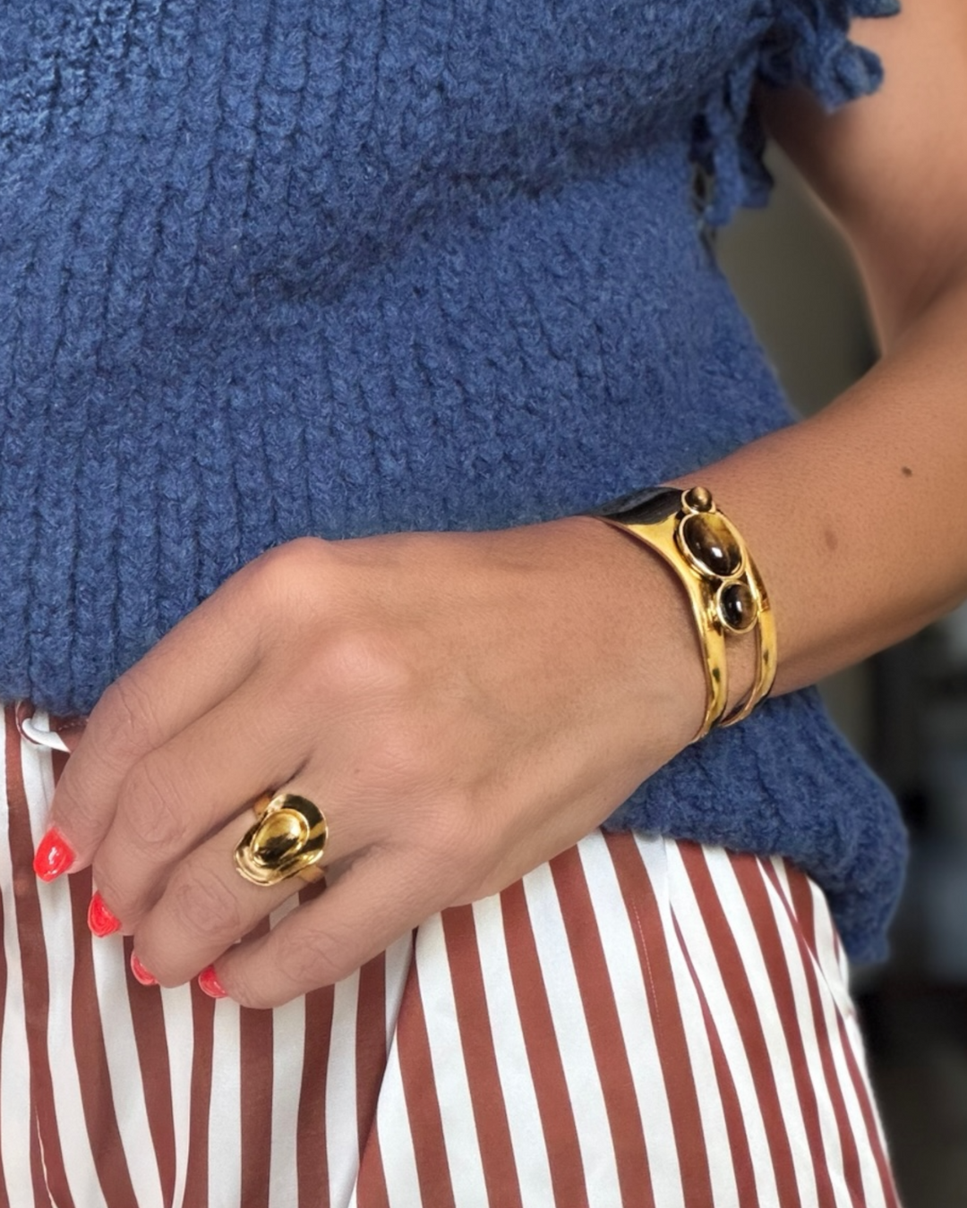 Gold tigers eye bracelet and ring on a person wearing a blue sweater and striped pants.